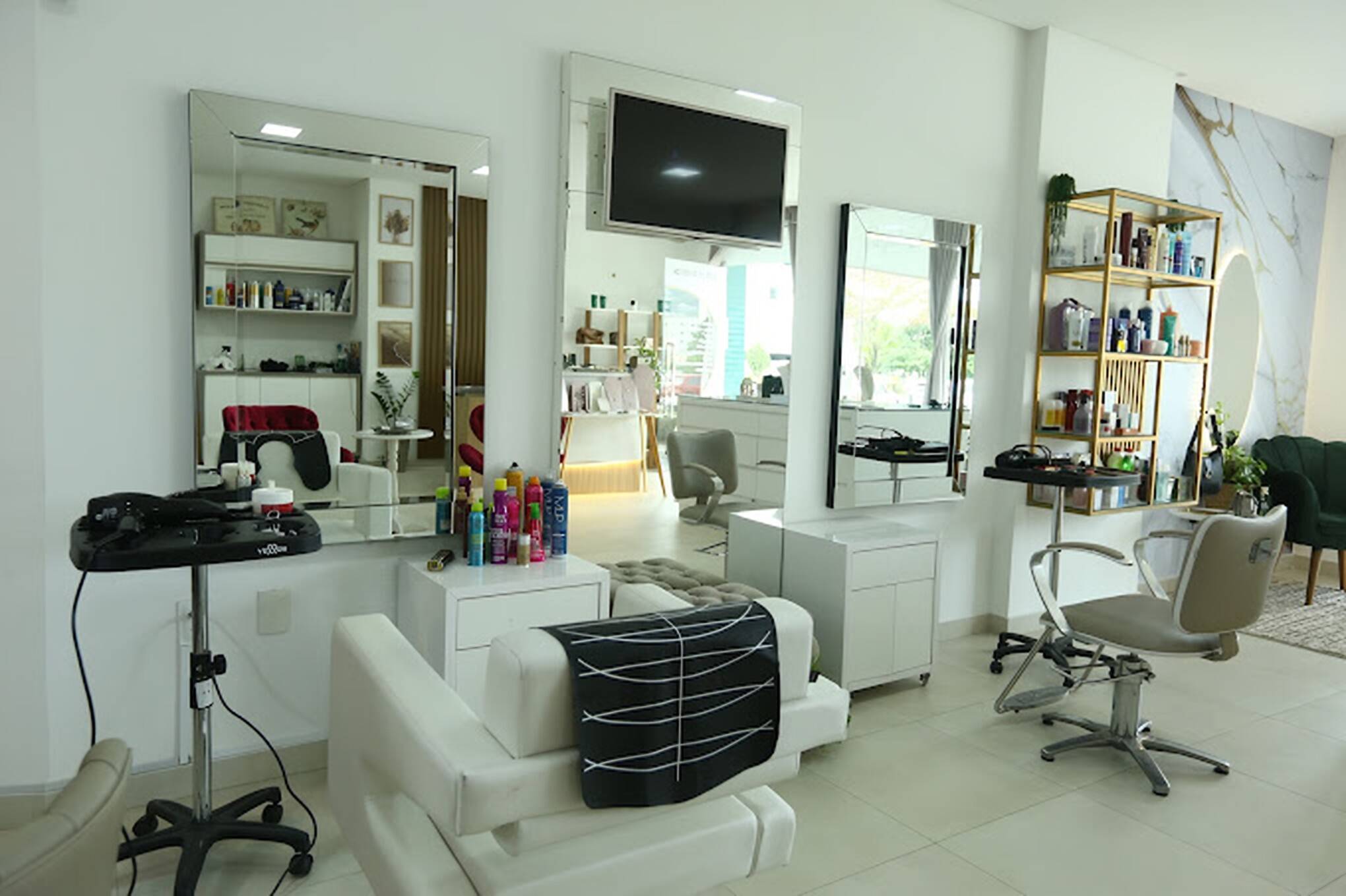 Interior do salão Essence Beauty Collective: bancadas com espelhos, cadeiras de atendimento claras, prateleira dourada com produtos e parede de mármore ao fundo.